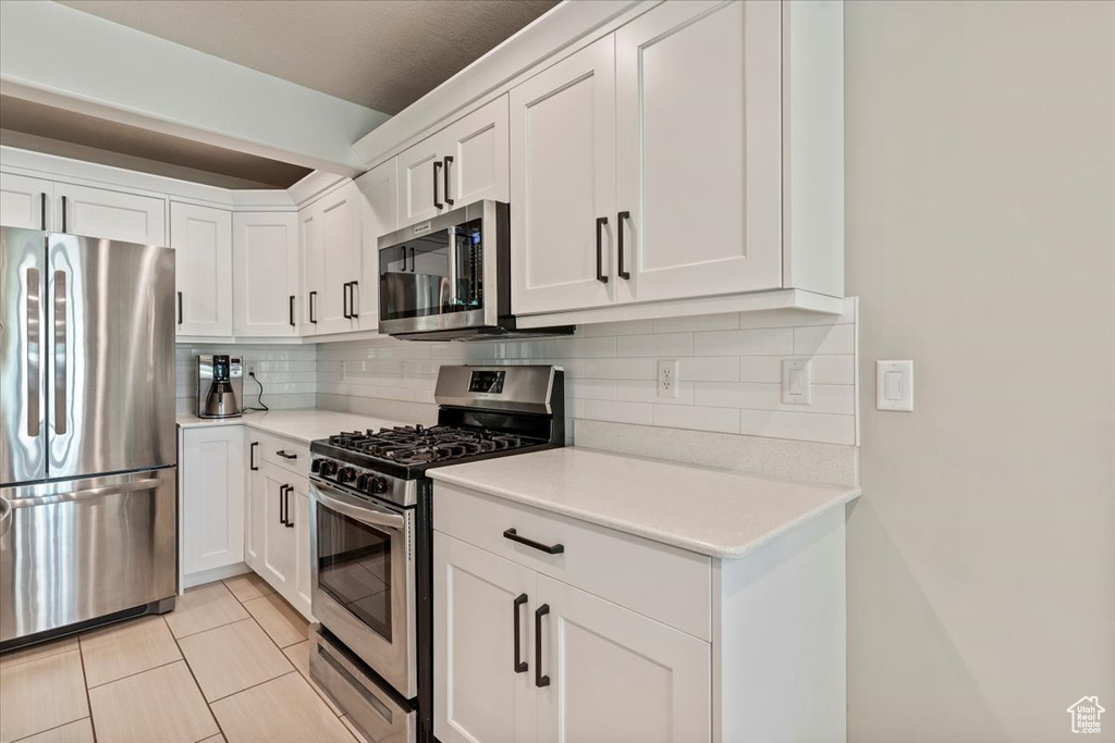 Kitchen featuring stainless steel appliances, white cabinetry, tasteful backsplash, and light countertops