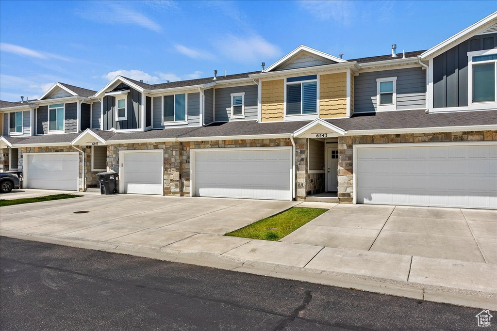 Multi unit property featuring a garage, driveway, and stone siding