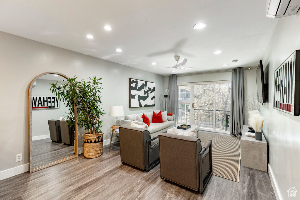 Living area with a wall mounted AC, a ceiling fan, light wood finished floors, and recessed lighting