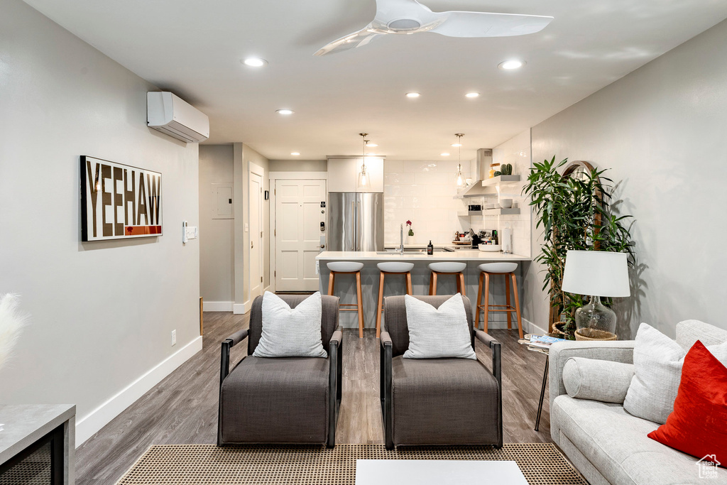 Living room with an AC wall unit, wood finished floors, recessed lighting, and ceiling fan