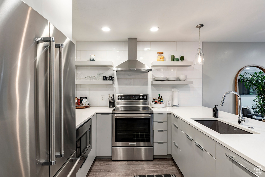 Kitchen with appliances with stainless steel finishes, open shelves, wall chimney range hood, backsplash, and light countertops