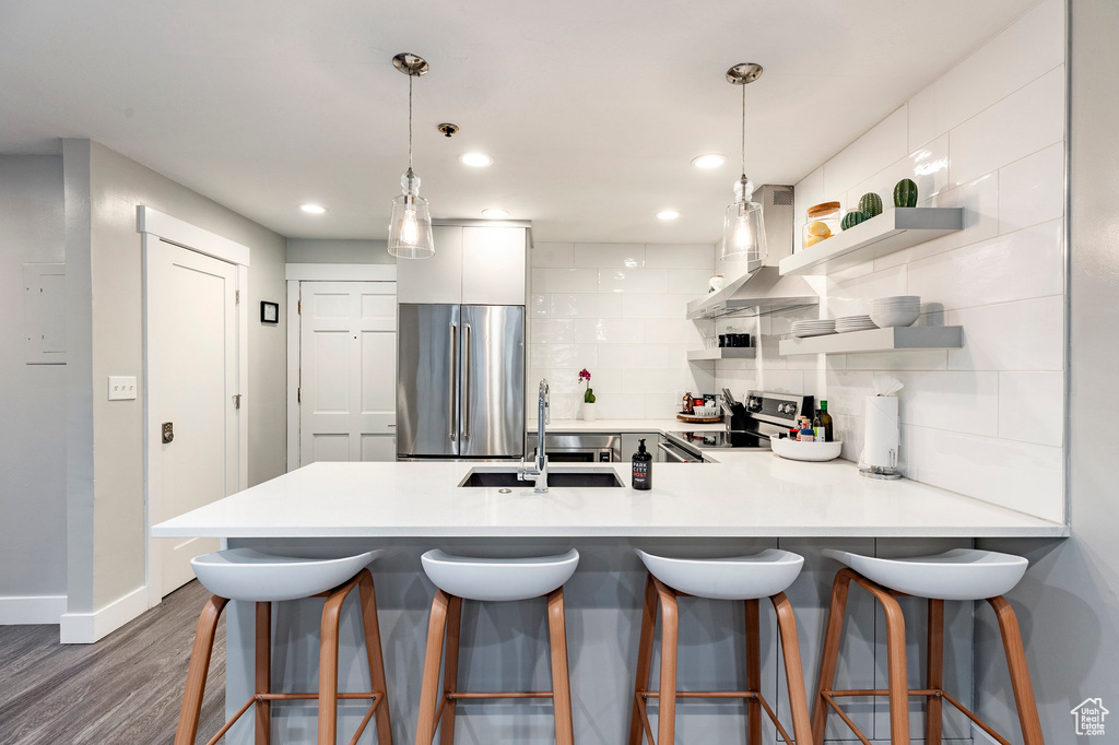 Kitchen featuring stainless steel appliances, wall chimney exhaust hood, a peninsula, dark wood-style floors, and light countertops