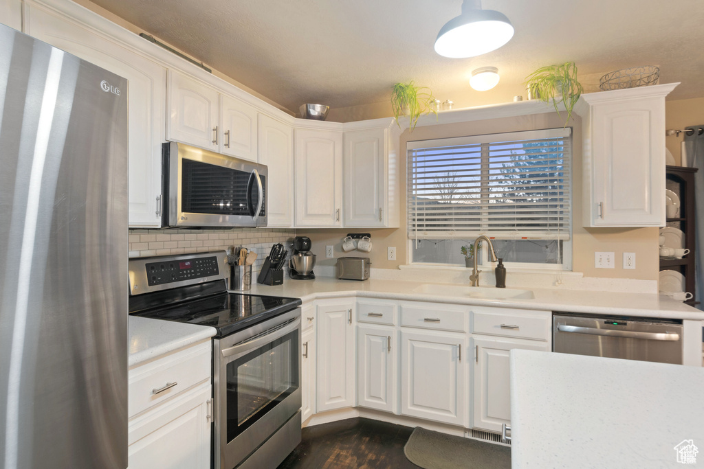 Kitchen featuring stainless steel appliances, white cabinetry, dark wood-type flooring, and light countertops
