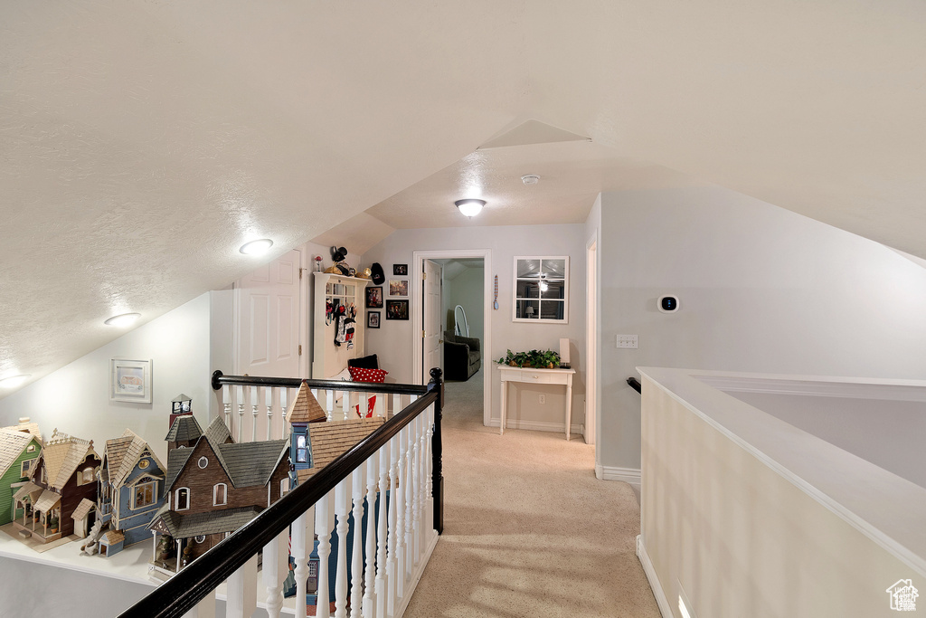 Hall with light colored carpet, an upstairs landing, vaulted ceiling, and a textured ceiling