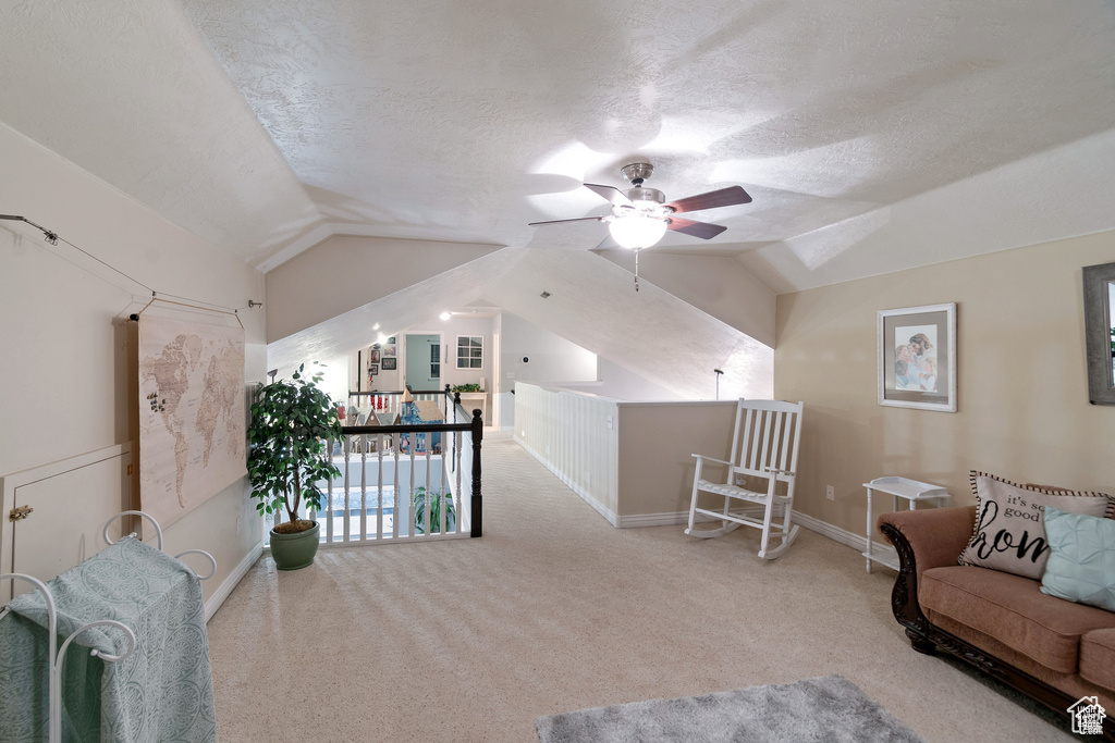 Living area with vaulted ceiling, ceiling fan, carpet, a textured ceiling, and an upstairs landing
