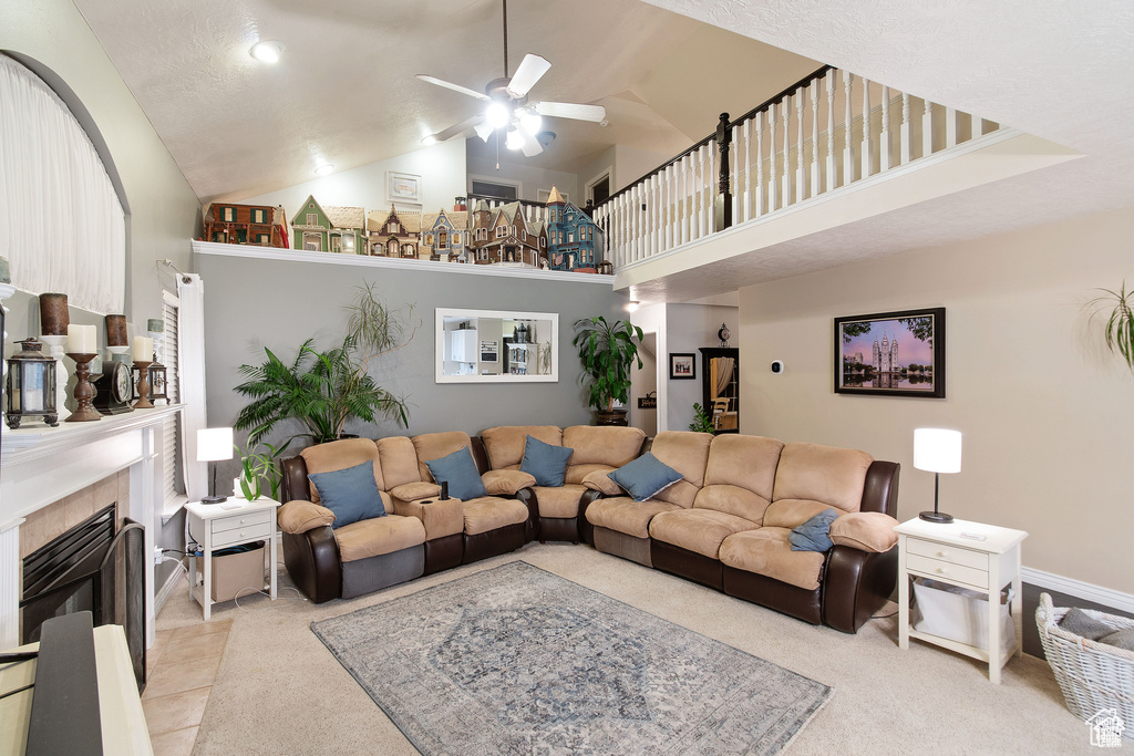 Living area featuring a ceiling fan, high vaulted ceiling, a tiled fireplace, and light carpet