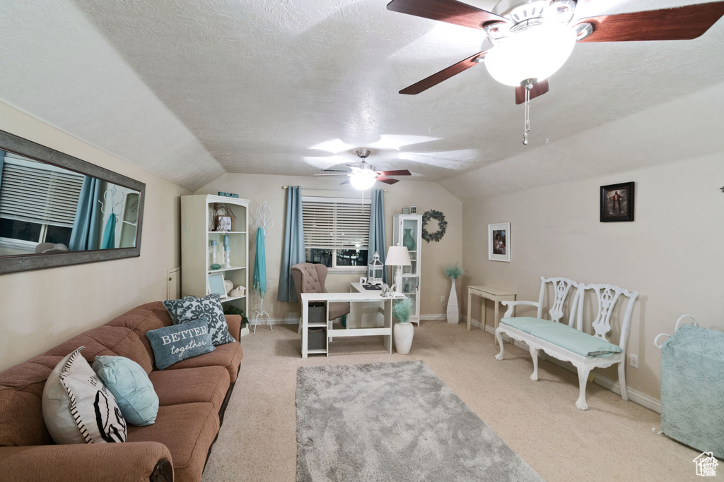 Carpeted living room featuring vaulted ceiling, ceiling fan, and a textured ceiling