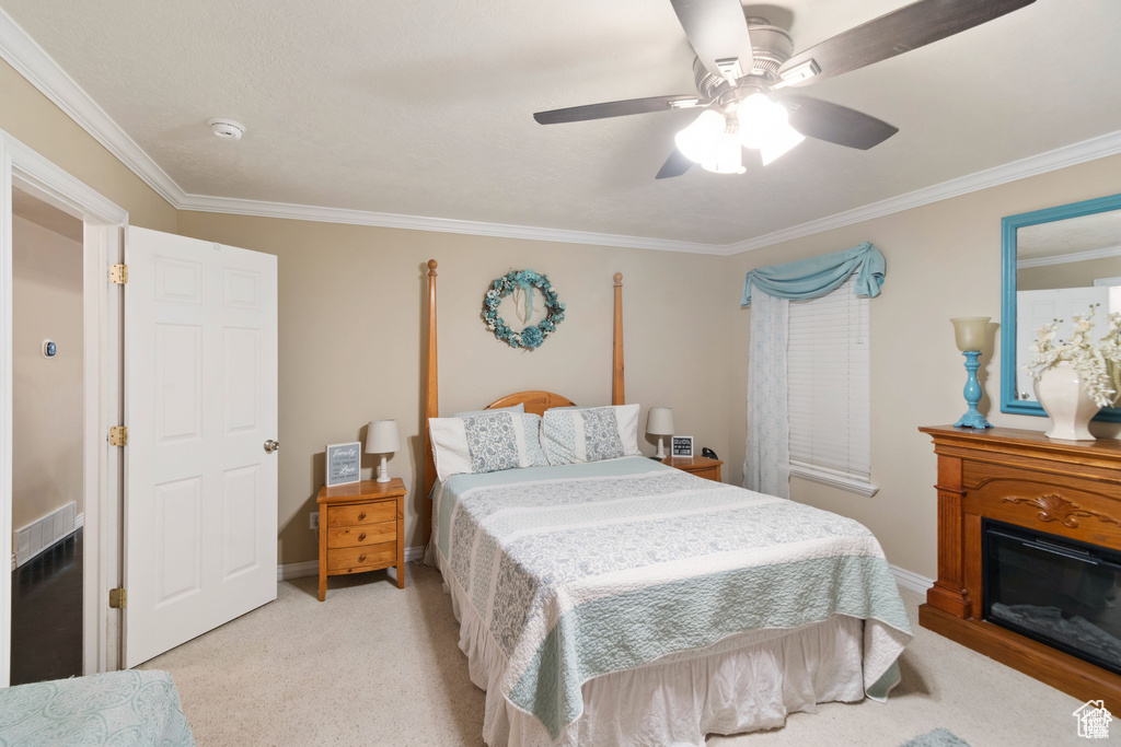 Bedroom featuring ornamental molding, a glass covered fireplace, ceiling fan, and carpet floors