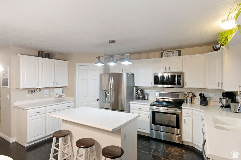 Kitchen featuring appliances with stainless steel finishes, dark wood-style flooring, a center island, decorative backsplash, and a breakfast bar area