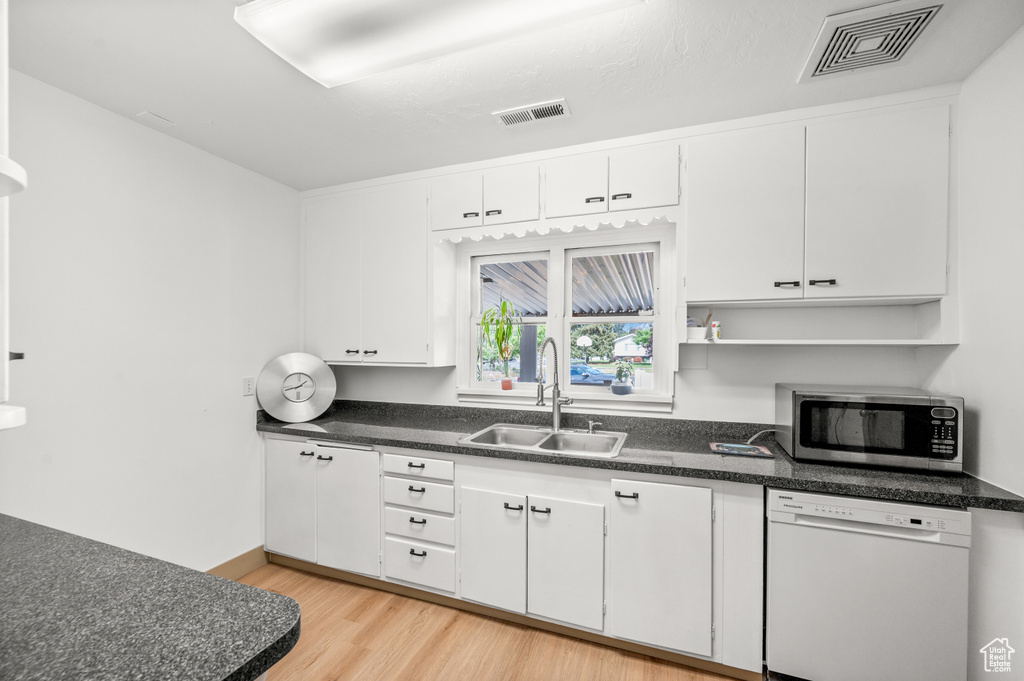 Kitchen featuring white dishwasher, stainless steel microwave, light wood-type flooring, white cabinets, and open shelves
