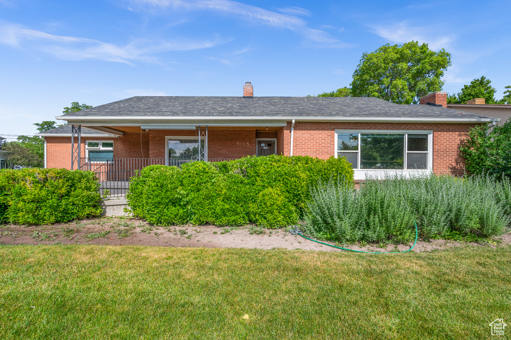 Ranch-style home featuring a chimney, brick siding, a front yard, and roof with shingles