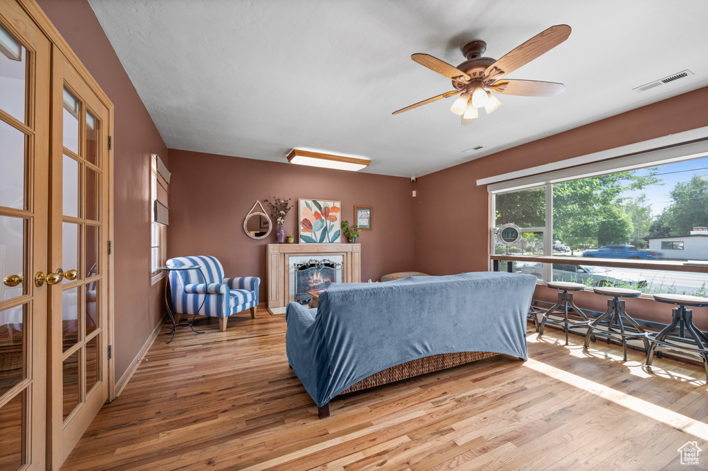 Living area featuring wood finished floors, a glass covered fireplace, a ceiling fan, and french doors