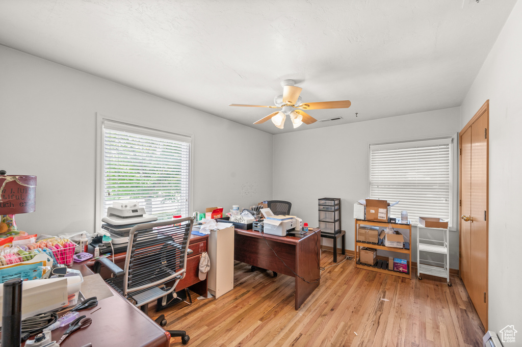 Office area with light wood finished floors, baseboard heating, and a ceiling fan