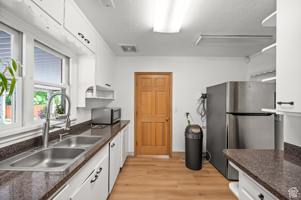Kitchen with appliances with stainless steel finishes, light wood-style floors, white cabinetry, and open shelves