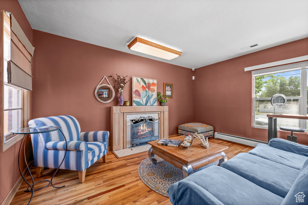 Living area with a baseboard heating unit, light wood-style flooring, and a fireplace with flush hearth
