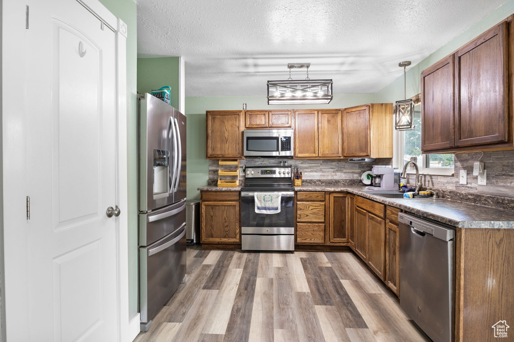 Kitchen with stainless steel appliances, dark countertops, a textured ceiling, wood finished floors, and brown cabinetry
