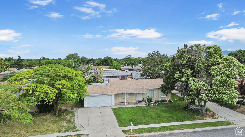 View of front of home featuring concrete driveway, a front lawn, brick siding, and view of wooded area