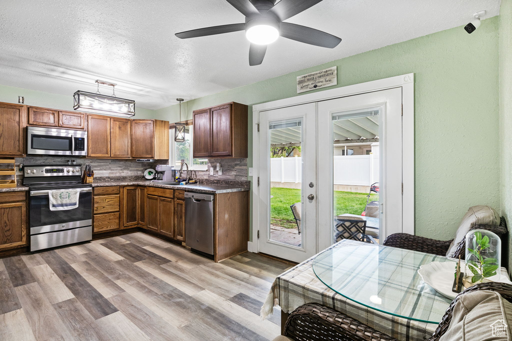 Kitchen with appliances with stainless steel finishes, french doors, backsplash, brown cabinetry, and dark countertops