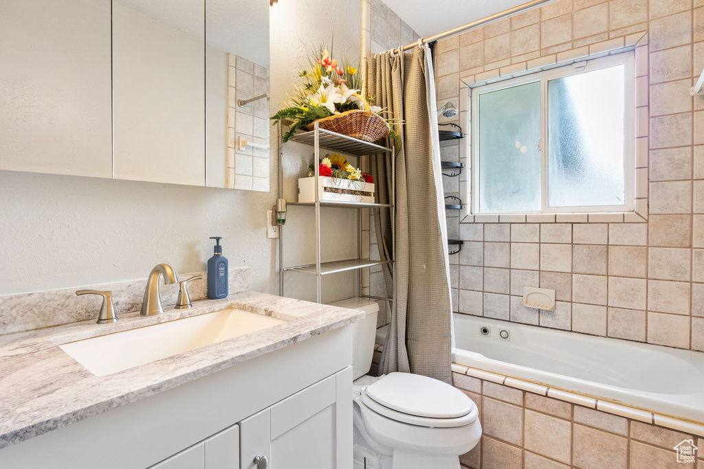 Full bath with tiled shower / bath combo, vanity, and a textured wall