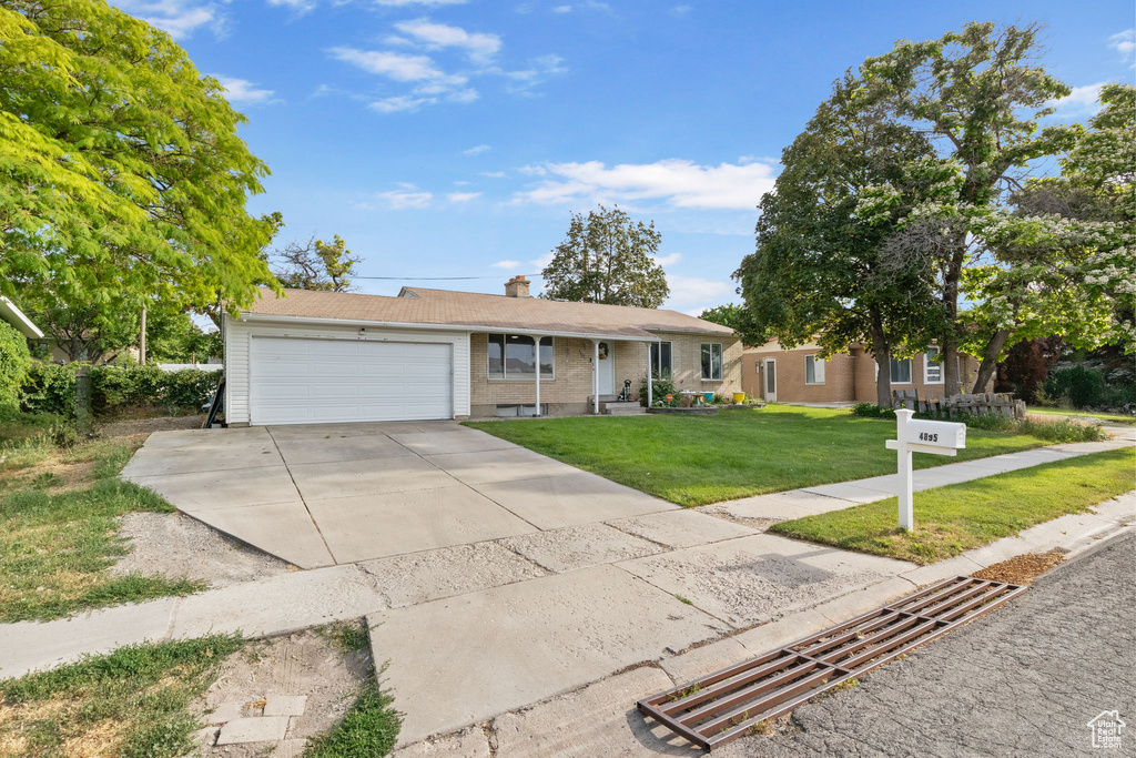 Ranch-style house with a garage, a front lawn, a chimney, concrete driveway, and brick siding