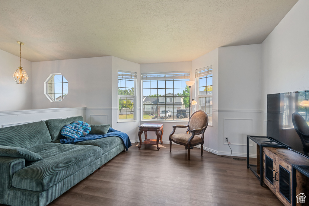 Living room featuring plenty of natural light, dark wood-type flooring, wainscoting, and a textured ceiling