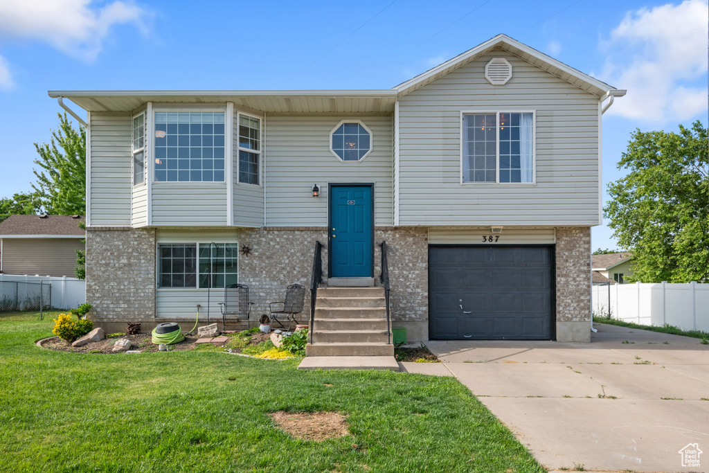 Raised ranch featuring a garage, driveway, and brick siding
