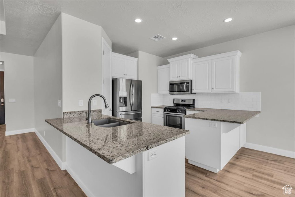Kitchen with appliances with stainless steel finishes, a peninsula, dark stone counters, light wood-type flooring, and white cabinets