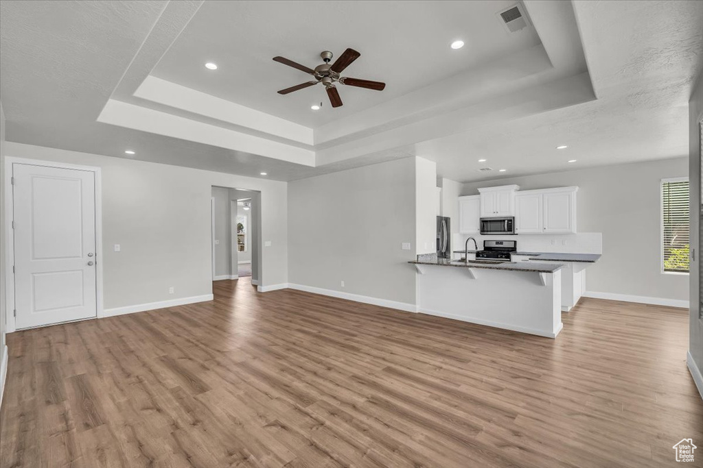 Unfurnished living room featuring a raised ceiling, a ceiling fan, light wood-style flooring, and recessed lighting