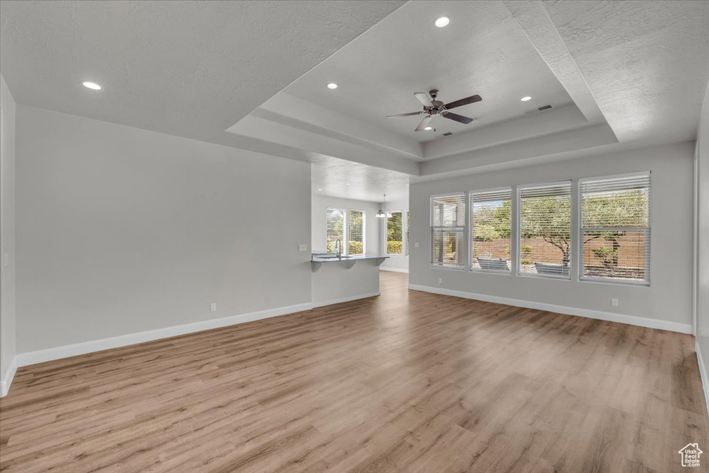 Unfurnished living room featuring a raised ceiling, light wood-style floors, ceiling fan, recessed lighting, and a chandelier