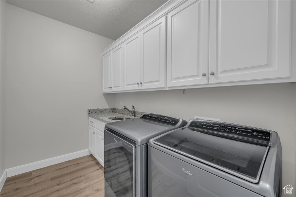 Laundry room with washing machine and dryer, cabinet space, and light wood-type flooring
