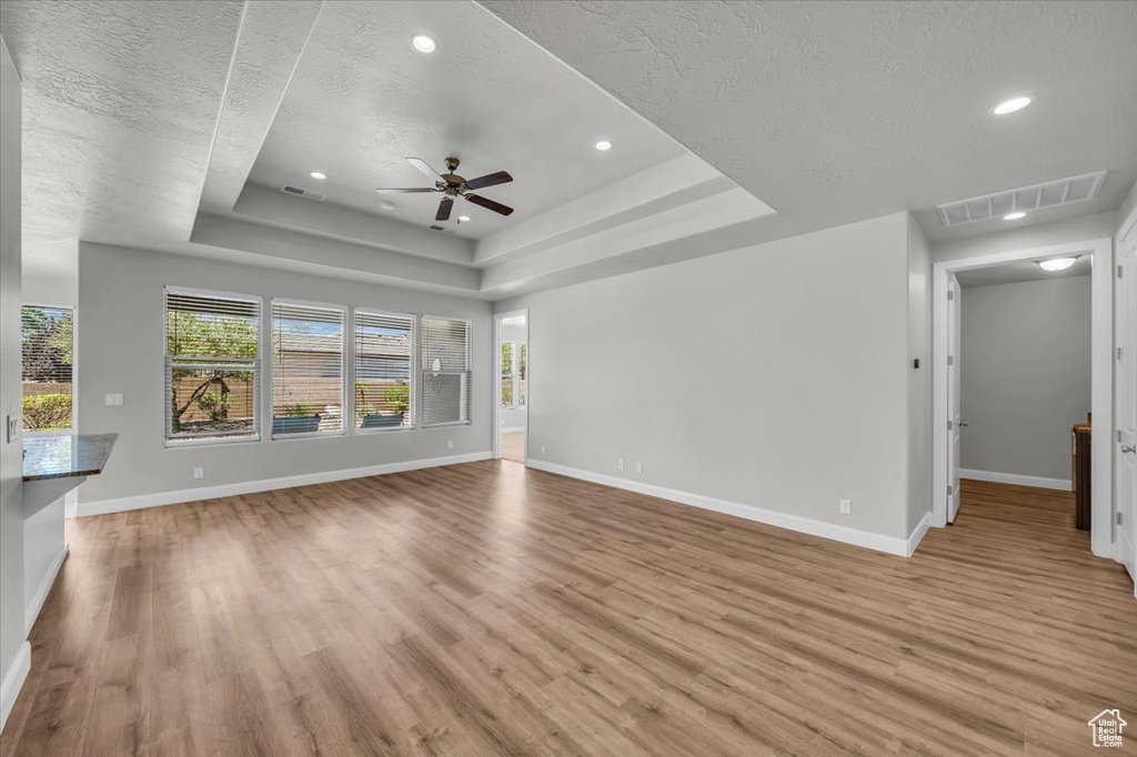 Unfurnished living room with a textured ceiling, light wood-type flooring, ceiling fan, a tray ceiling, and recessed lighting