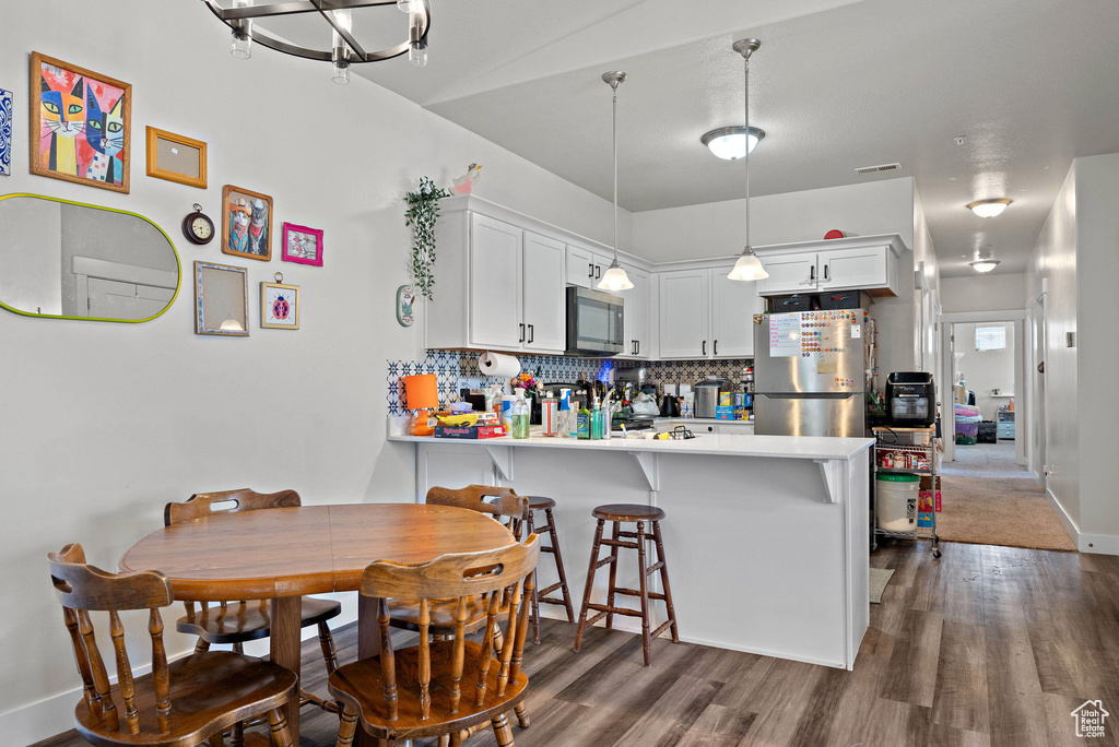 Kitchen with appliances with stainless steel finishes, dark wood-style floors, a peninsula, backsplash, and light countertops