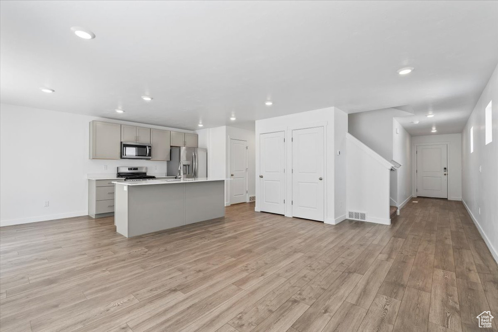 Kitchen featuring appliances with stainless steel finishes, gray cabinets, open floor plan, recessed lighting, and light wood-style floors