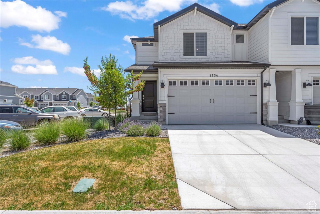 View of front of home with concrete driveway, stone siding, a garage, and a front yard