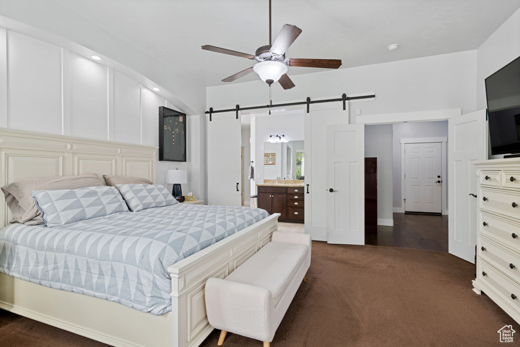 Bedroom with a barn door, dark colored carpet, a ceiling fan, and connected bathroom