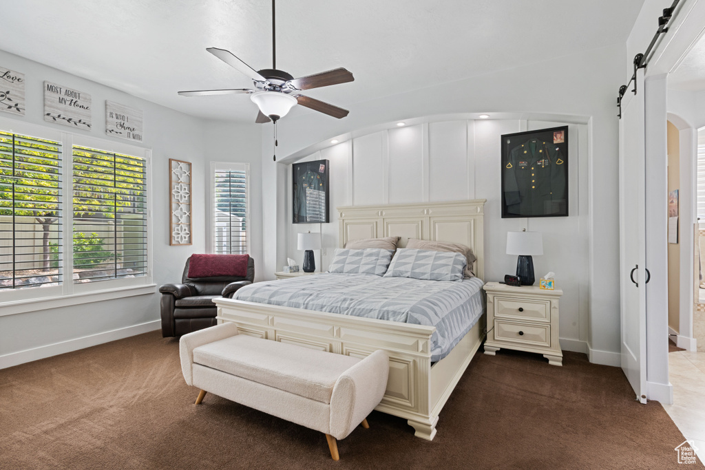 Bedroom with dark colored carpet, a barn door, arched walkways, and a ceiling fan