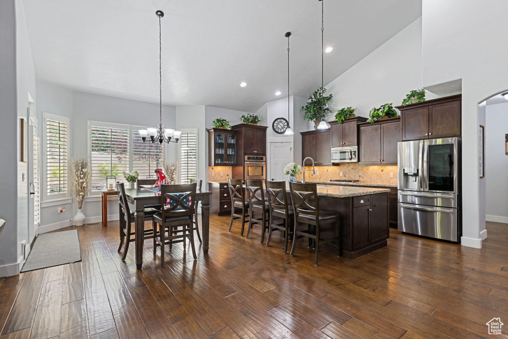 Dining room with a chandelier, dark wood finished floors, high vaulted ceiling, and recessed lighting