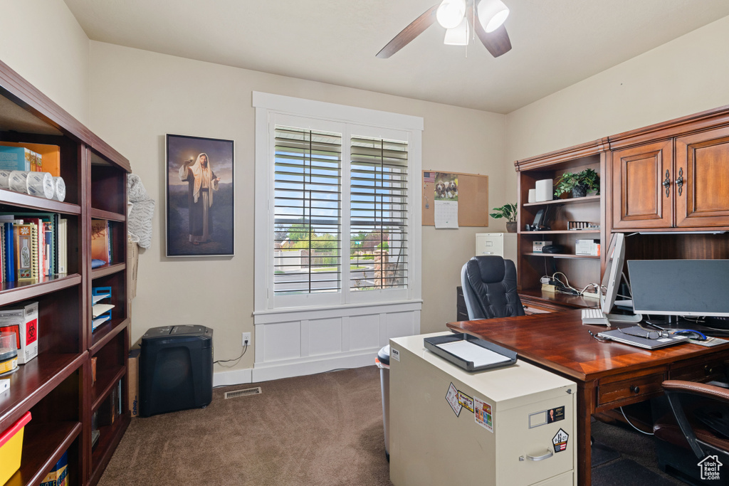 Home office with a ceiling fan and dark colored carpet