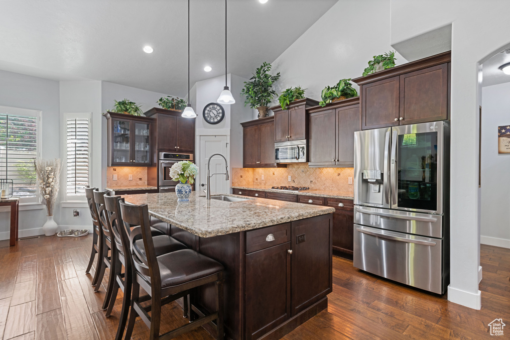 Kitchen featuring appliances with stainless steel finishes, backsplash, a kitchen bar, dark brown cabinetry, and recessed lighting
