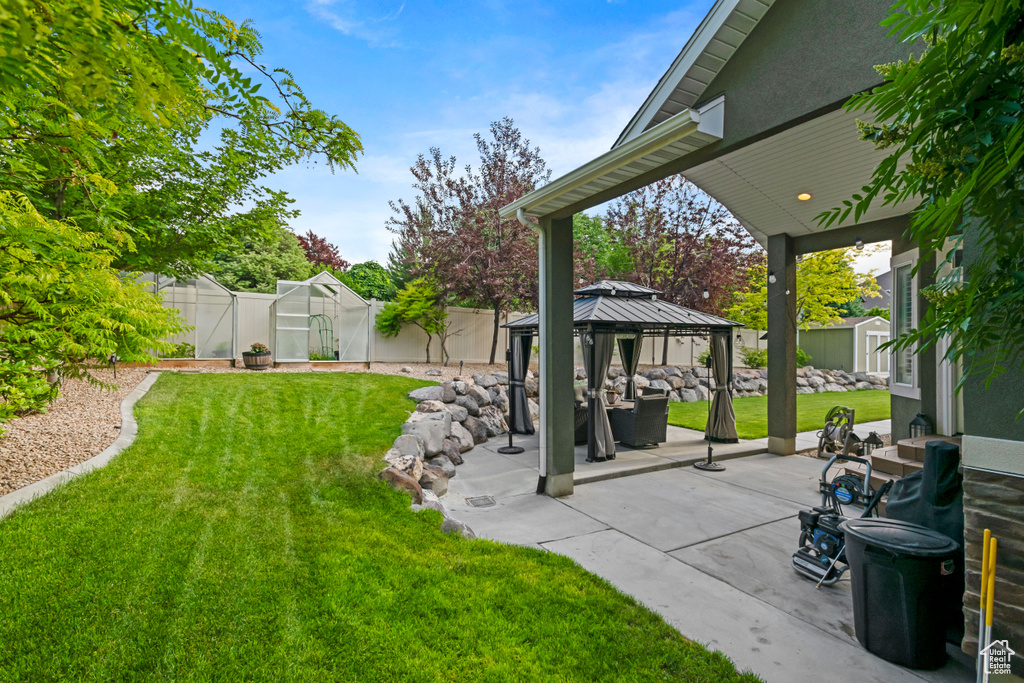 Fenced yard with a greenhouse, a gazebo, an outbuilding, and a patio area