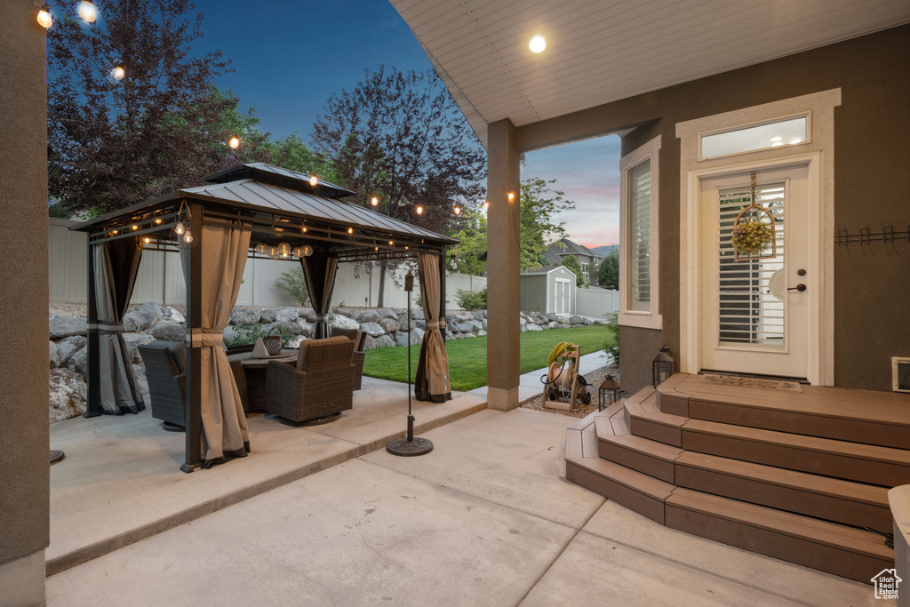 Patio terrace at dusk with outdoor lounge area, a patio, a shed, a fenced backyard, and a gazebo