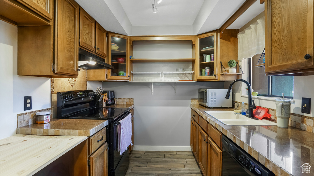 Kitchen with black appliances, under cabinet range hood, brown cabinetry, glass insert cabinets, and open shelves