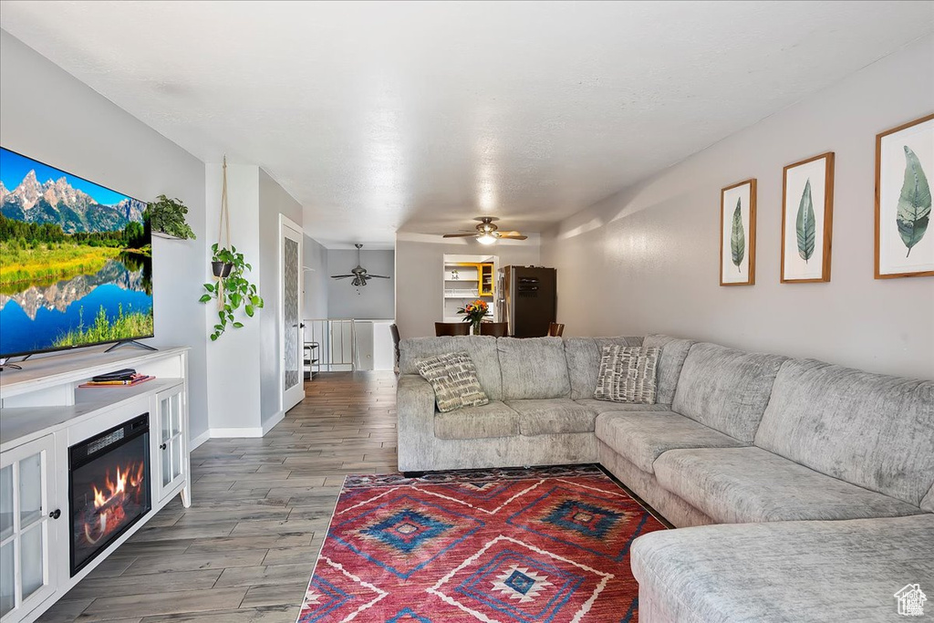 Living area with ceiling fan, wood finished floors, and a glass covered fireplace