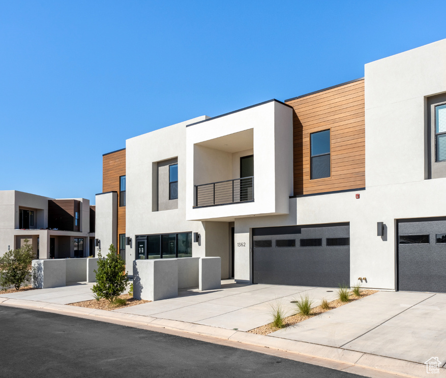 Contemporary house with an attached garage, stucco siding, concrete driveway, and a balcony