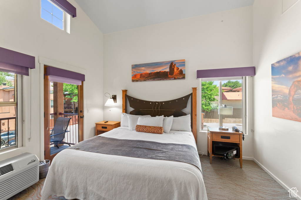 Bedroom with high vaulted ceiling, access to outside, multiple windows, and a wall mounted air conditioner