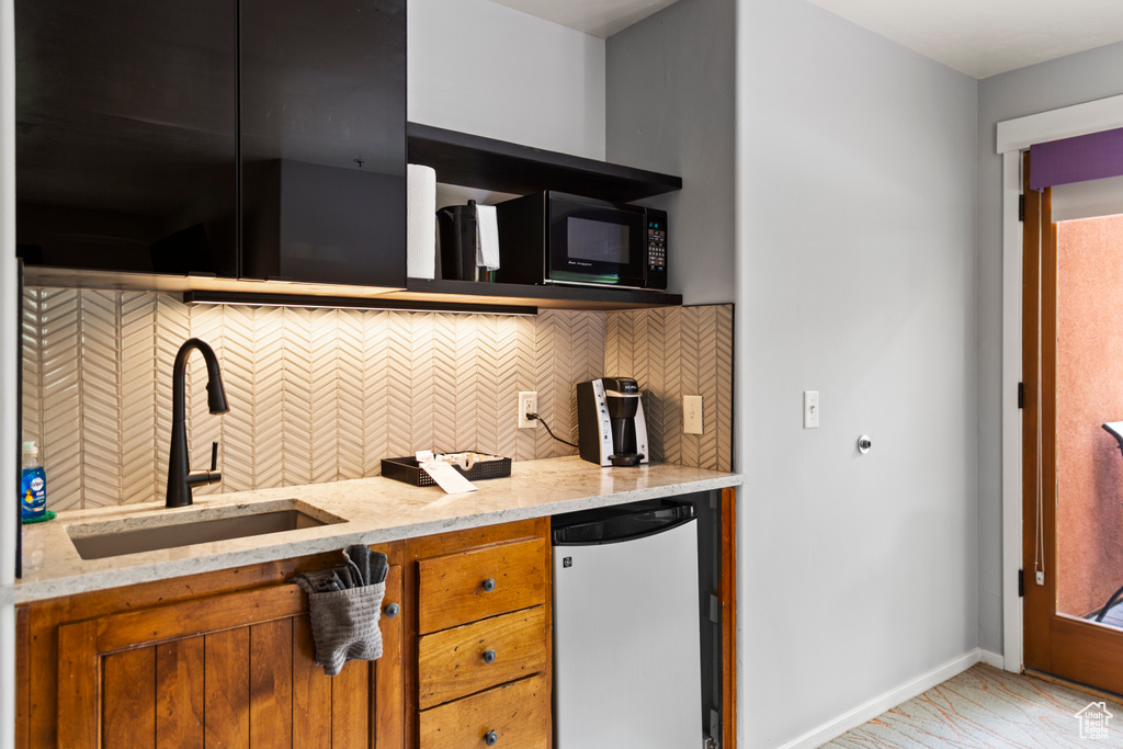 Kitchen with refrigerator, brown cabinetry, light stone counters, and decorative backsplash