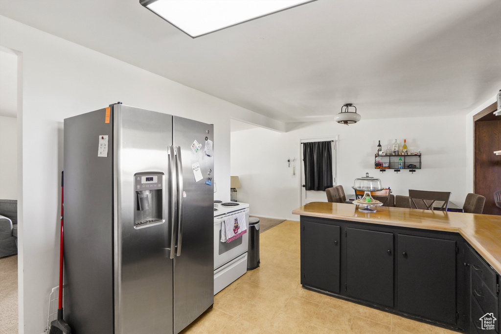 Kitchen with stainless steel fridge, white electric range, light countertops, dark cabinets, and open floor plan