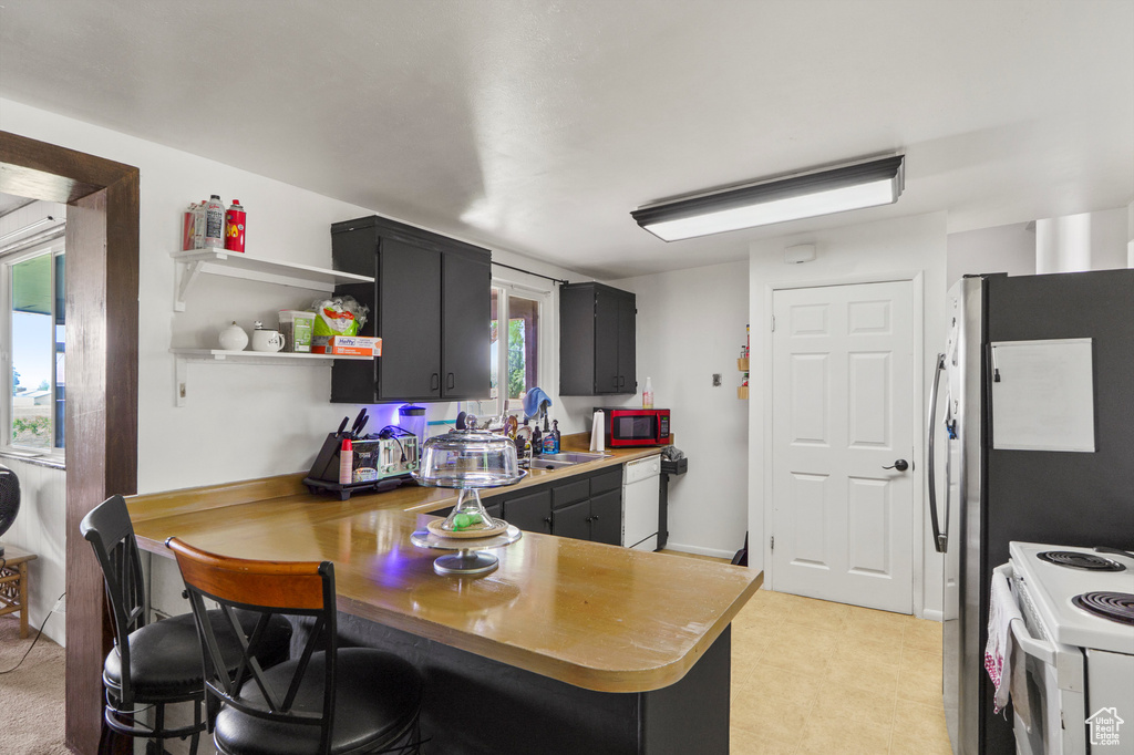 Kitchen featuring white appliances, a peninsula, dark cabinets, light countertops, and open shelves
