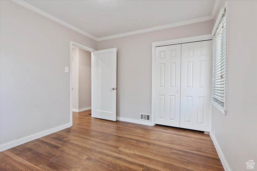 Unfurnished bedroom with wood finished floors, ornamental molding, and a closet