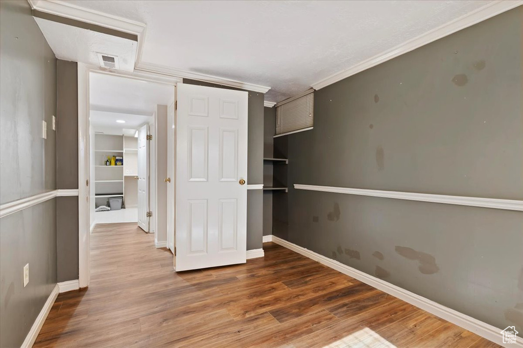 Unfurnished bedroom with wood finished floors, crown molding, and a closet